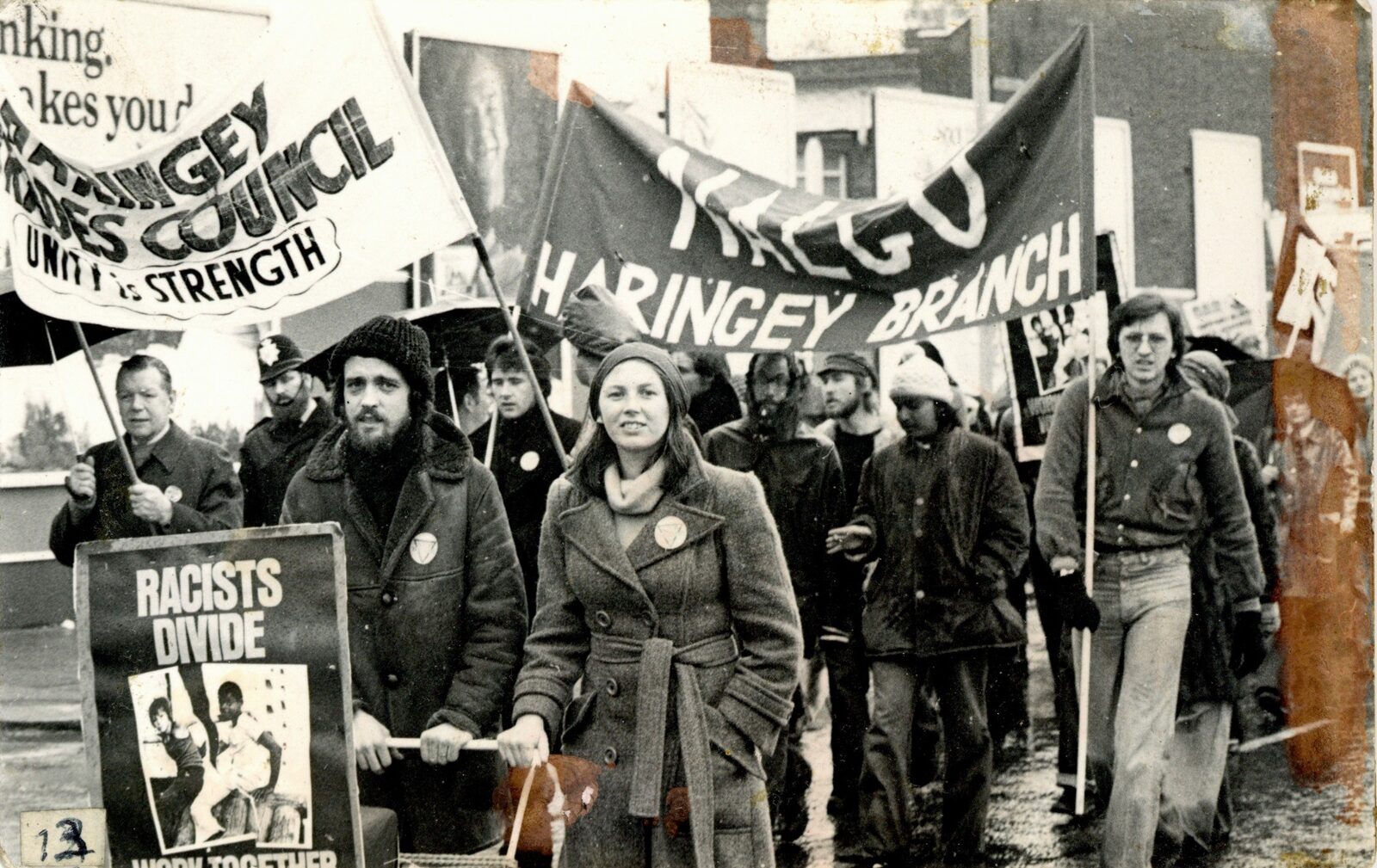 Black-and-white photograph of marchers behind Haringey Trades Council "Unity is strength" and NALGO Haringey Branch banners, one carrying a placard reading "Racists divide".